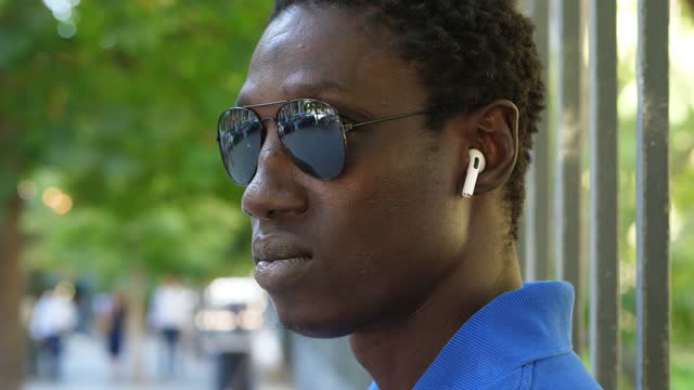 young african man wearing sunglasses puts on wireless headphones