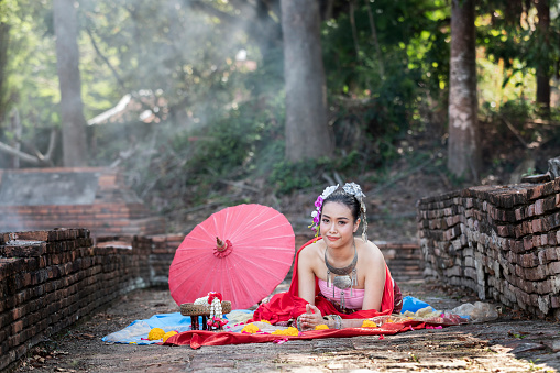Beautiful Thai woman wearing thai traditional clothing with red umbrella crouching on the floor in amid the smoke and fog.