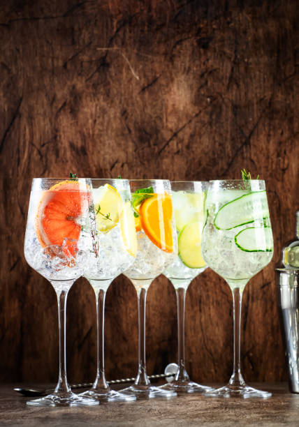 istock Gin and tonic cocktails set. Alcoholic drinks with lime, lemon, grapefruit, cucumber, soda and spicy herbs in wine glasses, wooden background. Summer cocktail party 1463837022
