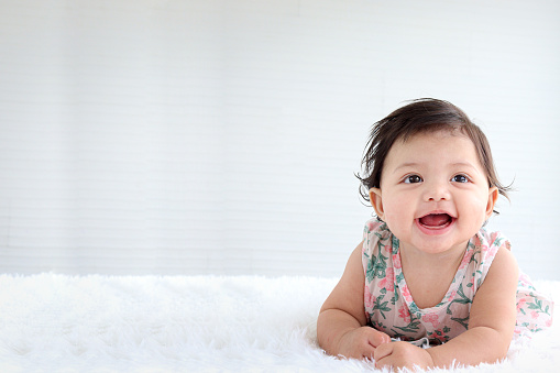 Portrait of six months crawling baby on fluffy white rug with copy space, happy smiling adorable sweet little girl kid lying on bed in bedroom, childhood and baby care concept