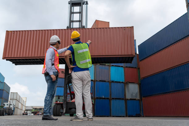 istock Industrial worker works with co-worker at overseas shipping container yard . Logistics supply chain management and international goods export concept . 1463840825