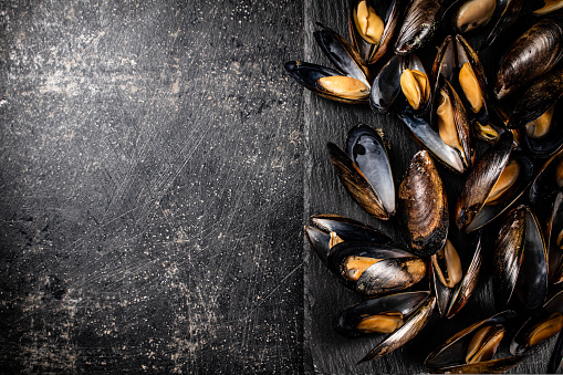 Delicious mussels on a stone board. On a black background. High quality photo