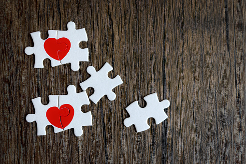 Two pieces of puzzle forming red heart on rustic brown wooden surface, heart on pieces of jigsaw, romantic background for celebrating anniversary on Valentine day, love unity of a couple in love couple.