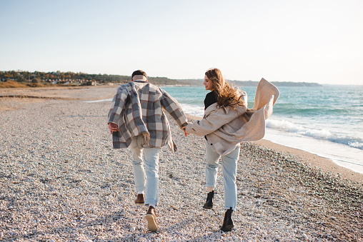 Happy love couple running at sea shore wear casual coat and denim pants. Freedom concept.