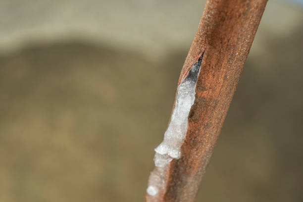 Looking down on a ruptured frozen copper water line with a puddle on the basement floor stock photo