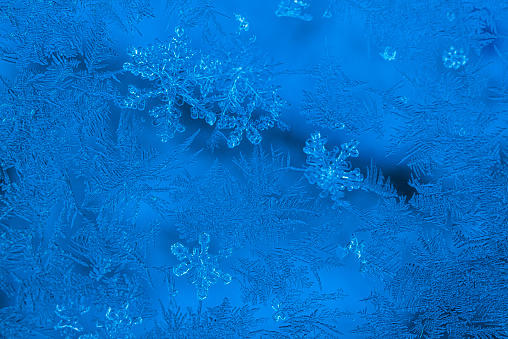 A few snowflakes among the frost pattern on a window on a cold winter morning