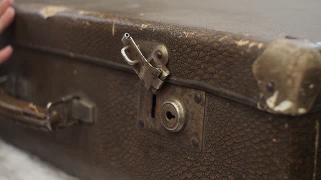 A woman's hand opens the lock on an old leather suitcase. A retro suitcase stands on an armchair. A woman's hand opens the locks on the lid of a suitcase.