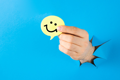 Human hand holding yellow speech bubble with smiley face on blue background