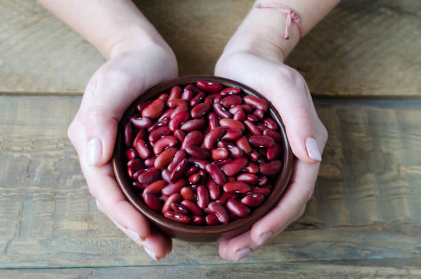 Female hands hold a brown bowl with red beans on a wooden background. The concept of vegetarian food. Rustic style. Horizontal orientation. stock photo