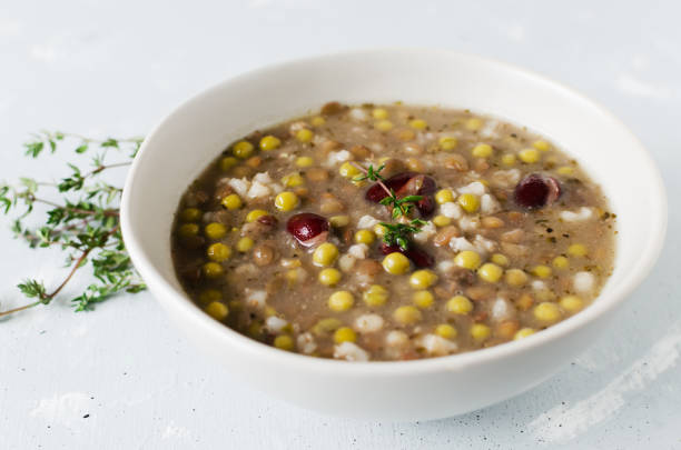Bean soup in a ceramic gray bowl with a sprig of thyme and a piece of bread on a grey background. A mix of red beans, lentils and peas. The concept of vegetarian food. Horizontal orientation. stock photo