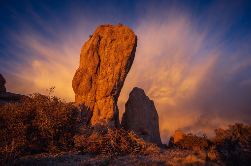 Massive boulder illuminated by sunset on mountain ridge with explosive cloud glowing orange in The McDowell Sonoran Preserve