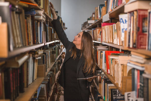 istock Smiling librarian takes a book from the shelf while holding digital tablet in her hands 1463856878