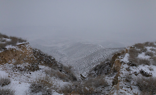 View of a mountain range on a foggy snowy winter day. Mountains partially covered in mist.