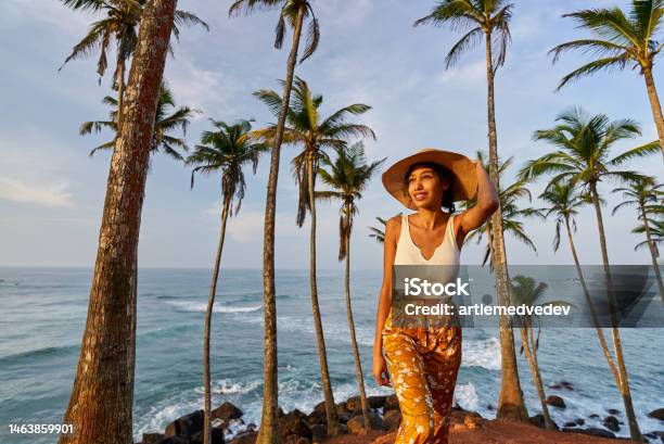 Young African Female Model Posing In Colorful Clothes At Tropical Location At Sunrise Black Woman Against Exotic Scenery At Dawn Multiracial Darkskinned Model Poses In Front Of Palm Trees At Sunset Stock Photo - Download Image Now