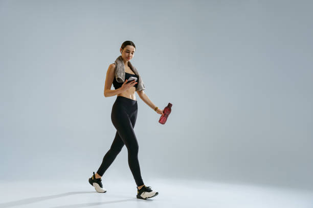istock Woman use phone while walking with water bottle and towel around her neck over studio background 1463866032