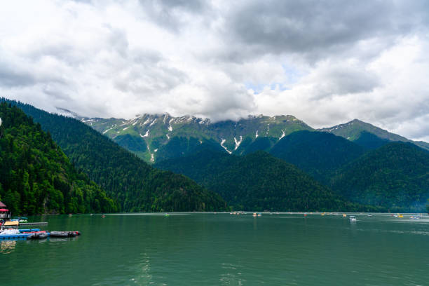 alpensee ritsa. touristen auf katamaran, die entlang des sees zwischen bergen segeln. - italian lake district stock-fotos und bilder