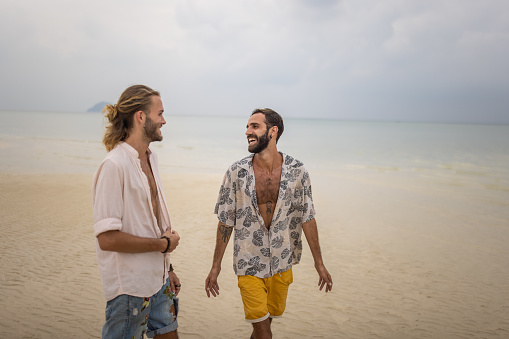 Two men, happy gay couple taking a walk on the beach by the sea in Thailand.