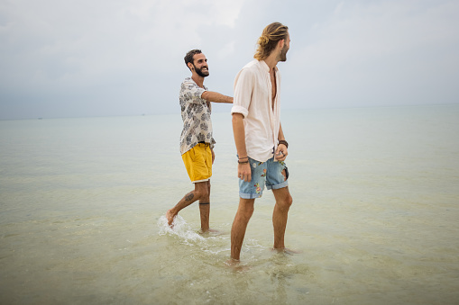 Two men, happy gay couple having fun in the shallow part of the sea in Thailand.