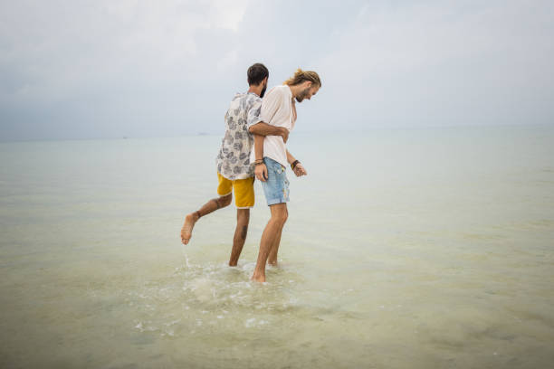 Two men, happy gay couple having fun in the shallow part of the sea in Thailand.