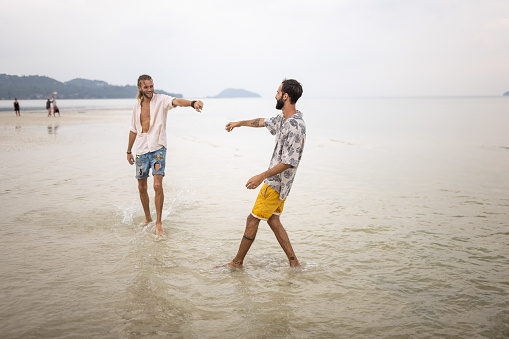 Two men, happy gay couple enjoying on the beach by the sea in Thailand.