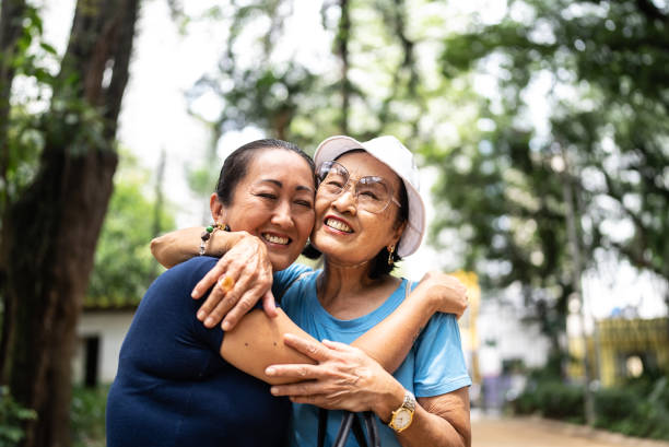 madre e figlia che abbracciano il parco pubblico - senior adult asian ethnicity family women foto e immagini stock