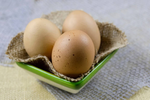 Three boiled hen's eggs are on a piece of linen cloth and have been so placed in a small ceramic bowl