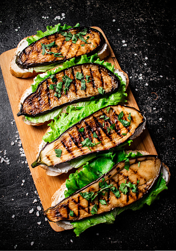 Sandwich with grilled eggplant and lettuce on a wooden cutting board. On a black background. High quality photo