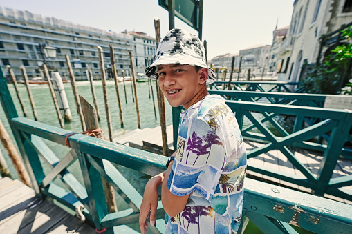 Boy tourist wear panama stand and wait in wooden gondola dock, Venice, Italy.