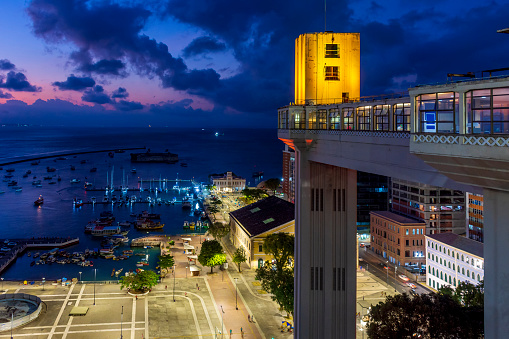 Facade of the famous Lacerda elevator illuminated at night with city and boats in background in Salvador city, Bahia
