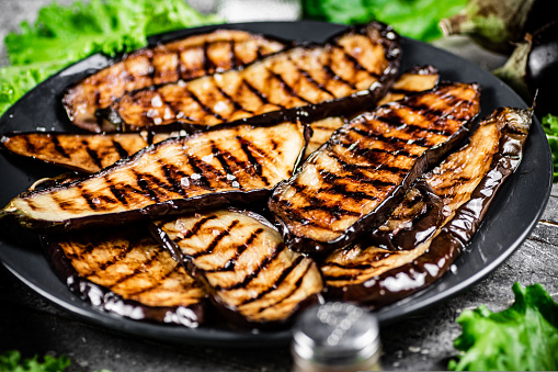 Grilled pieces of eggplant on a plate of lettuce. On a gray background. High quality photo