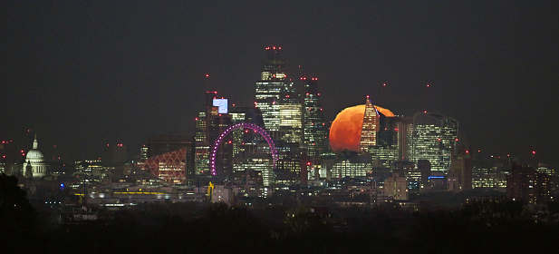 Full moon rising over the London cityscape.  From Richmond Park (eleven miles distance) the  perspective in a rare and spectacular phenomenon makes the moon look very large and red as it emerges just after sunset. No image manipulation