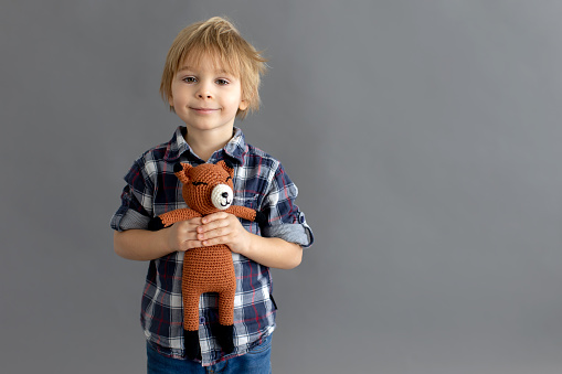 Portrait of one Happy toddler boy playing with his teddy bear at home in front of Gray wall.