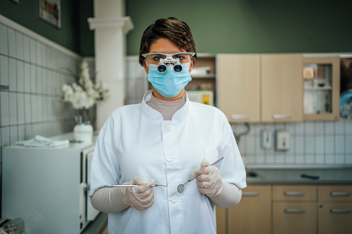 Young female dentist with microscope glasses and dental equipment tools in dental office