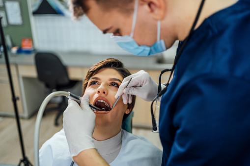 Male dentist repairing the teeth of a a young woman at the dental office