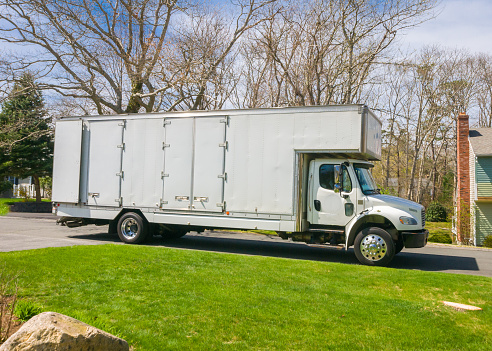 A parked white moving van with its rear doors open being loaded on an April afternoon on Cape Cod
