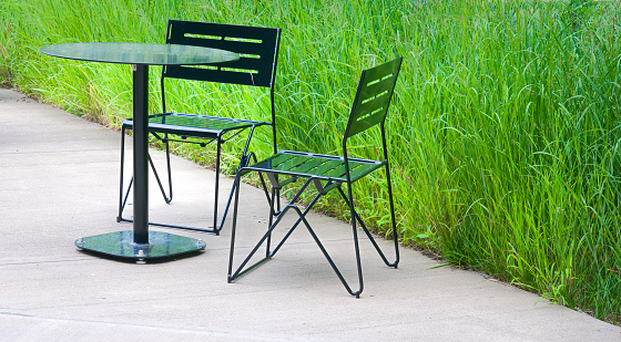 An outdoor metal table and two chairs with a background of summer grasses.