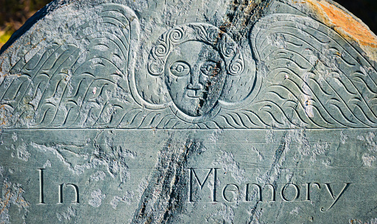 Ancient gravestone on Cape Cod depicting a smiling winged cherub  and the words \