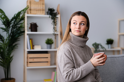 Portrait of thoughtful winter clothing pretty woman holding cup of hot drink like coffee or tea