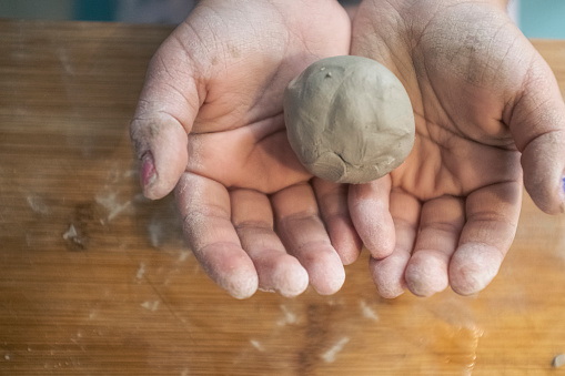 Ball made of clay being mashed by dirty kids hands while playing on a wooden table close up still