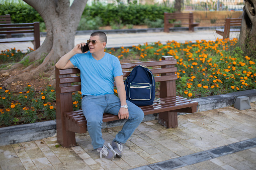 Asian business man relaxing in the park after work. He looking phone enjoying the shadow of the tree in a sunny day. businessman relieving, rest time concept