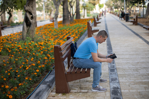 Young man is sitting on a street bench in Valletta and looking at his mobile phone.