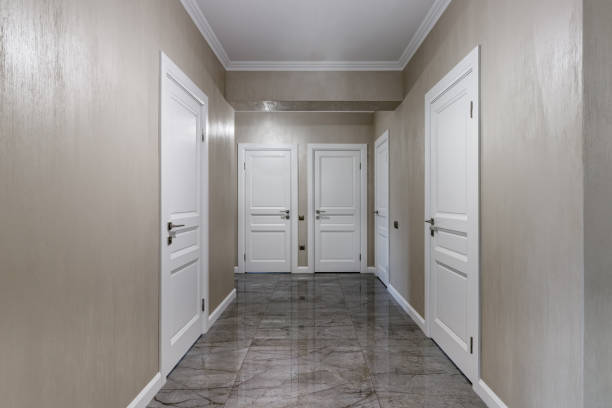 Corridor with white walls and doors in an apartment with a marble floor.