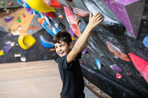 A cute boy climber is smiling at someone while about to climb at the bouldering gym