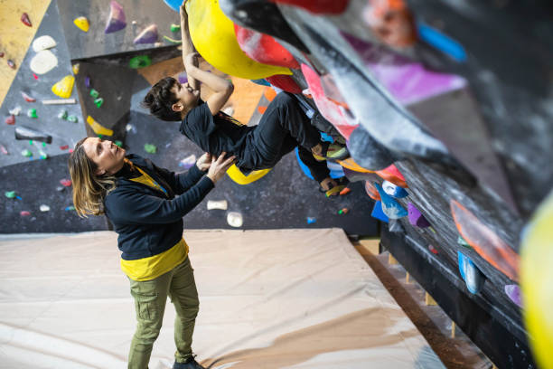 um treinador de escalada ajudando um menino alpinista a resolver um problema de pedra de parede de laje - climbing wall rock climbing holding reaching - fotografias e filmes do acervo