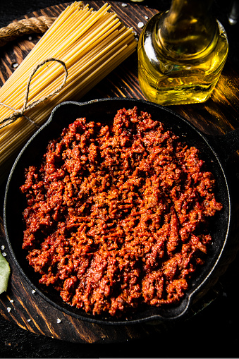 Bolognese sauce in a frying pan with a bunch of pasta dry. Against a dark background. High quality photo