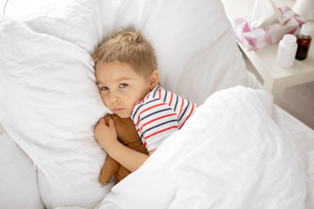 istock Sweet blond preschool child with teddy bear, lying in bed sick, 1463898653