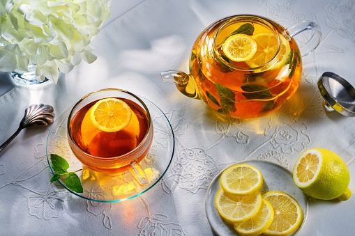 Mint and lemon tea on the table with a white tablecloth and a teapot in the background. Horizontal photo.