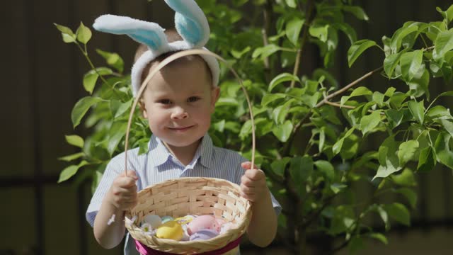 Easter boy portrait: cute kid boy Easter bunny ears holding basket Easter eggs