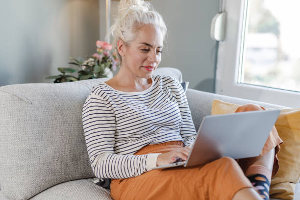 istock Mature woman relaxing on the sofa and using a laptop 1463902675