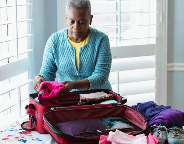 Senior African-American woman packing suitcase on table